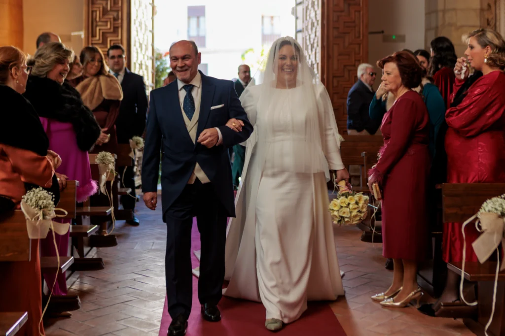 Novia entrando a la iglesia del brazo de su padre durante una boda religiosa en Jaén con invitados emocionados.