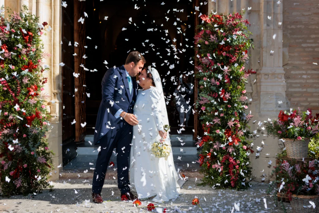 Novios besándose bajo una lluvia de pétalos a la salida de la iglesia en Jaén tras su ceremonia de boda.