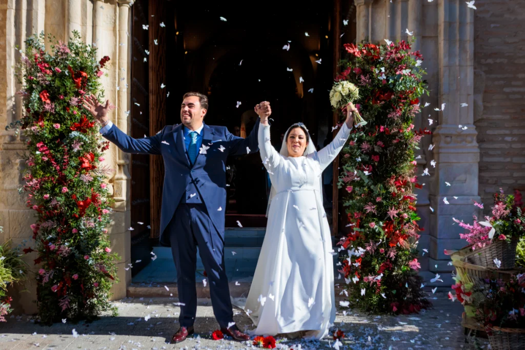 Novios saliendo de la iglesia en Jaén con los brazos levantados mientras caen pétalos tras la ceremonia.