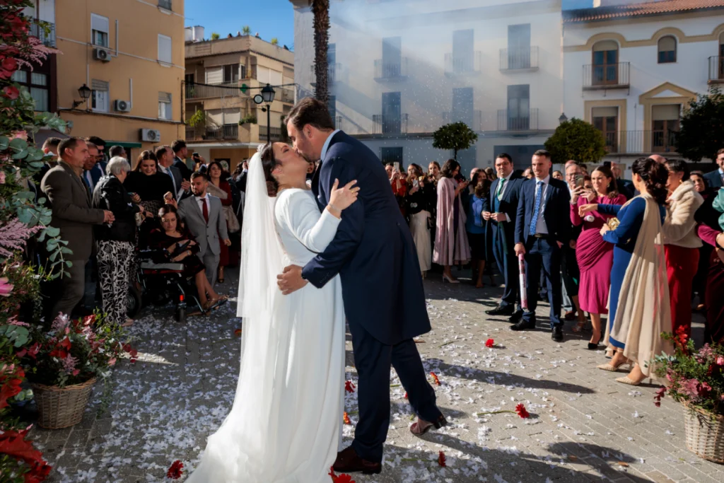 Novios besándose a la salida de su boda en una plaza de Jaén mientras los invitados lanzan pétalos.