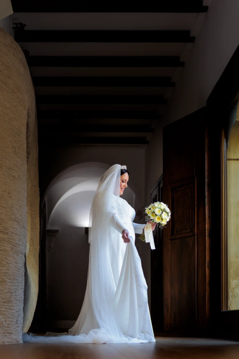 Novia con vestido y ramo junto a la ventana durante los preparativos de boda en Jaén