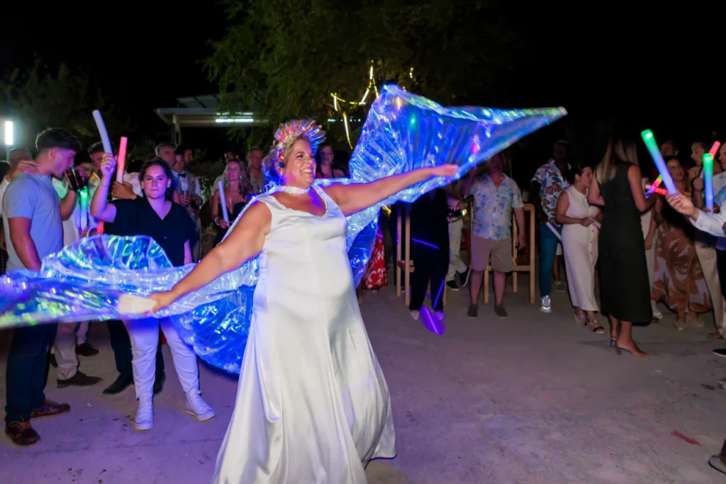 Novia bailando con alas luminosas durante la fiesta de boda al aire libre en Jaén rodeada de invitados.