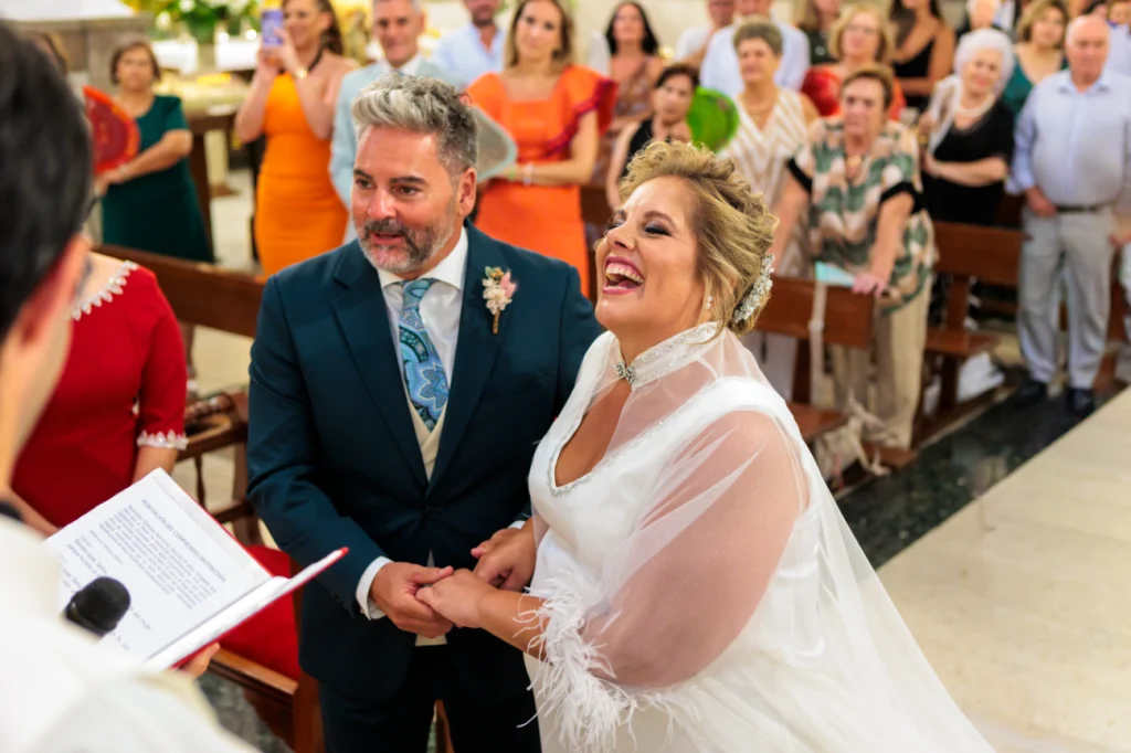 Novios sonriendo emocionados durante la ceremonia religiosa en una iglesia de Jaén con invitados al fondo.