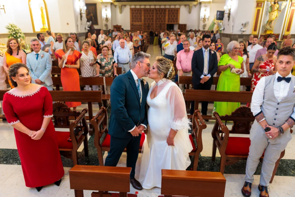Novios besándose durante la ceremonia religiosa en una iglesia de Jaén con invitados de fondo.