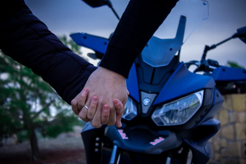 Manos de pareja entrelazadas delante de una moto deportiva azul en sesión fotográfica romántica.