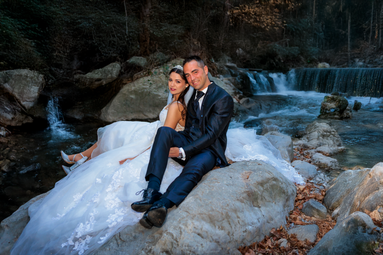 Novios sentados sobre rocas junto a una cascada durante una sesión postboda en la naturaleza en Jaén.
