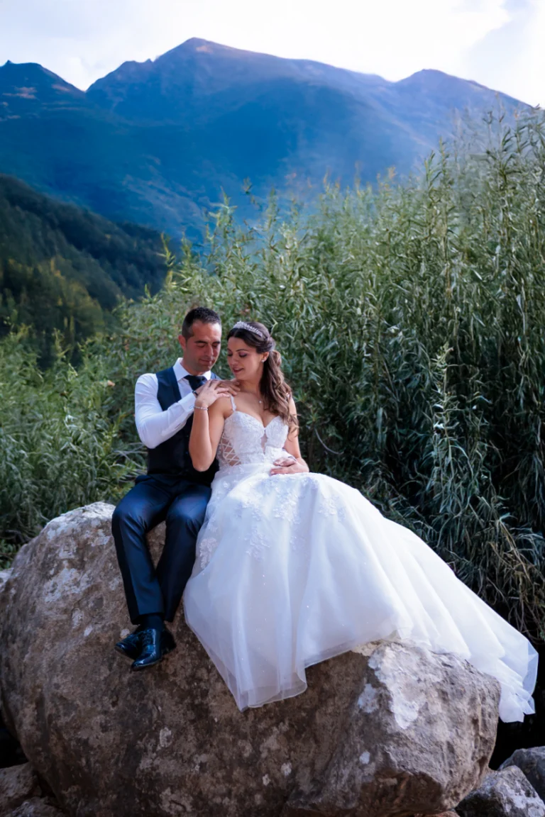 Novios sentados sobre una roca abrazados con paisaje de montaña al atardecer en Jaén.