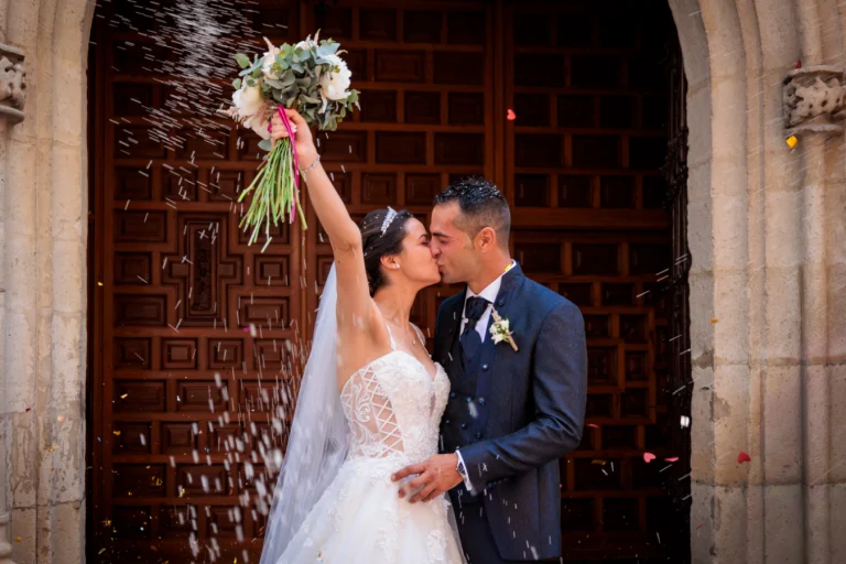 Novios besándose mientras lanzan arroz a la salida de la iglesia tras su boda en Jaén.